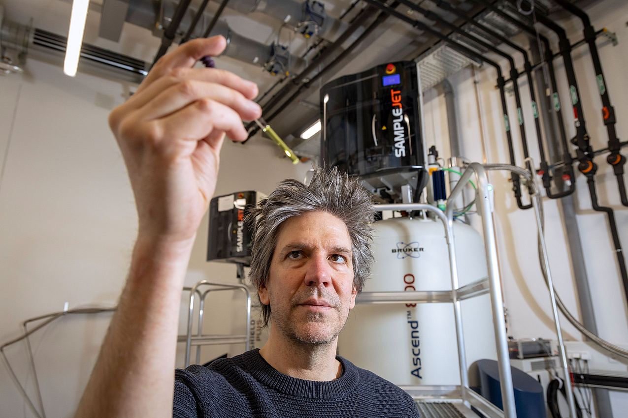 Forscher Tobias Madl steht in einem Kellerraum mit einem Gerät im Hintergrund  und begutachtet eine Probe