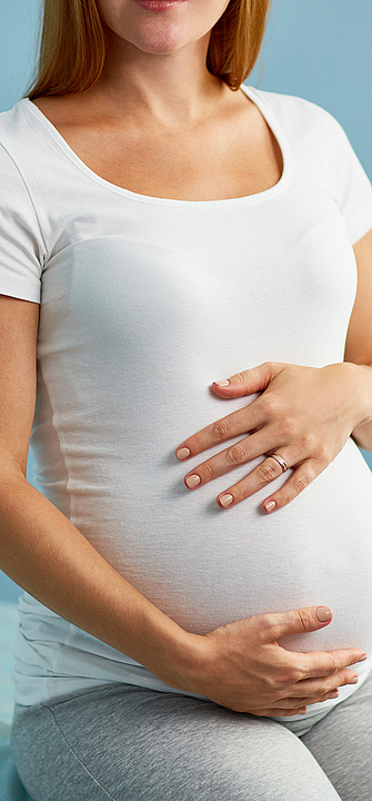 Schwangere Frau, die die Hände auf den Bauch gelegt hat und mit ihrem Frauenarzt spricht