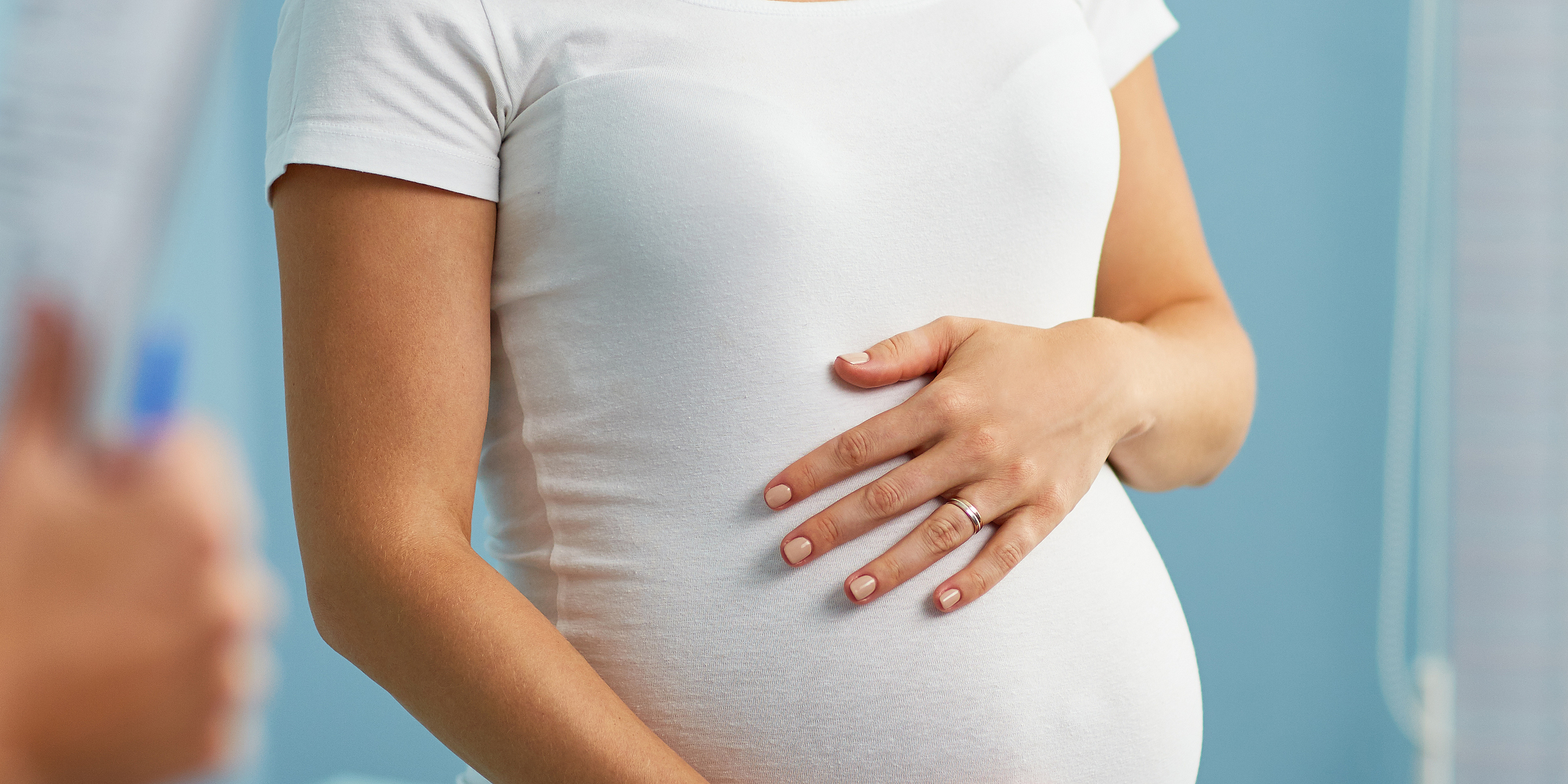 Schwangere Frau, die die Hände auf den Bauch gelegt hat und mit ihrem Frauenarzt spricht