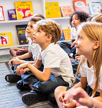 Eine Gruppe von Kindern sitzt am Boden und hören jemandem zu, der einen Vortrag hält