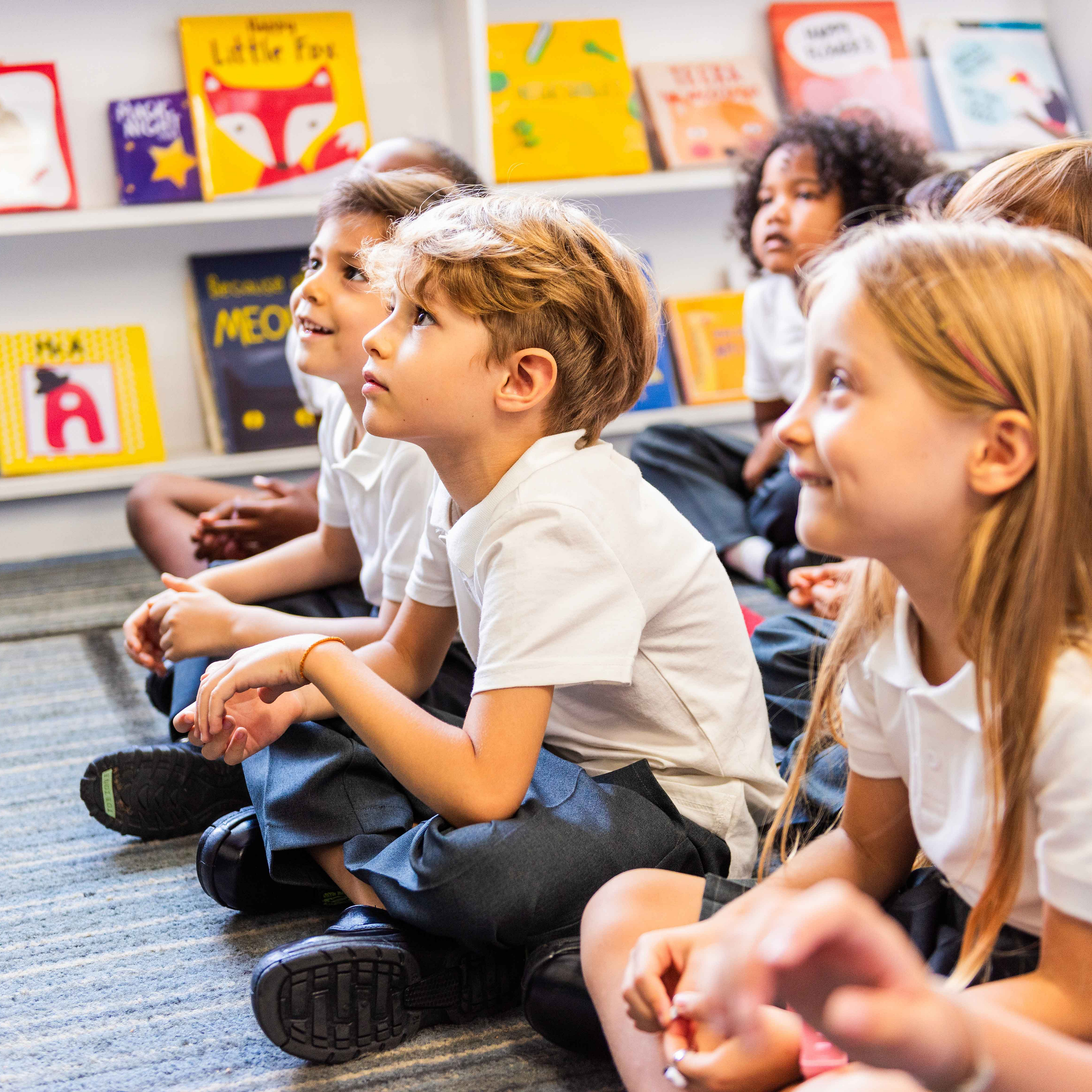 Eine Gruppe von Kindern sitzt am Boden und hören jemandem zu, der einen Vortrag hält