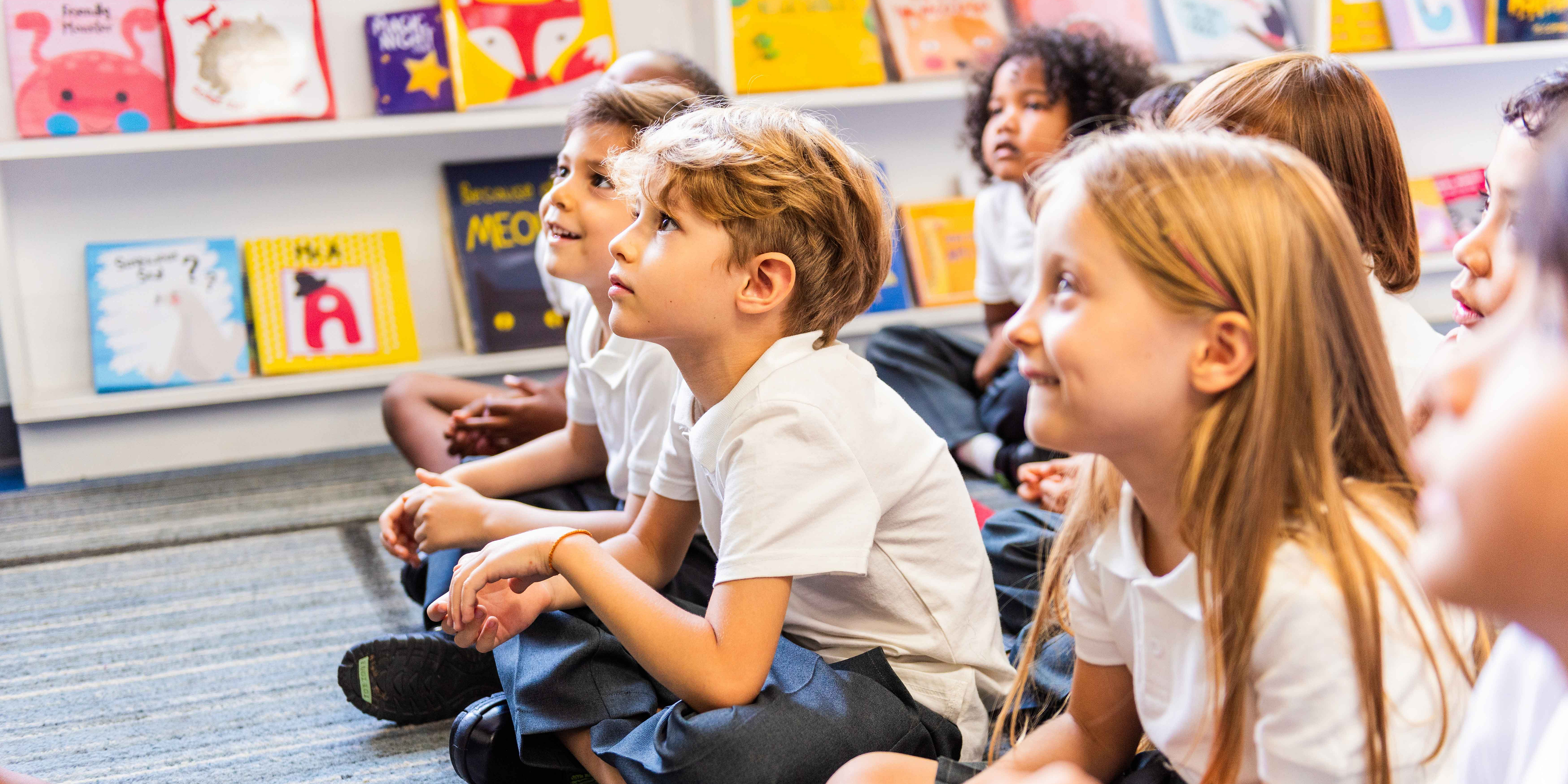 Eine Gruppe von Kindern sitzt am Boden und hören jemandem zu, der einen Vortrag hält