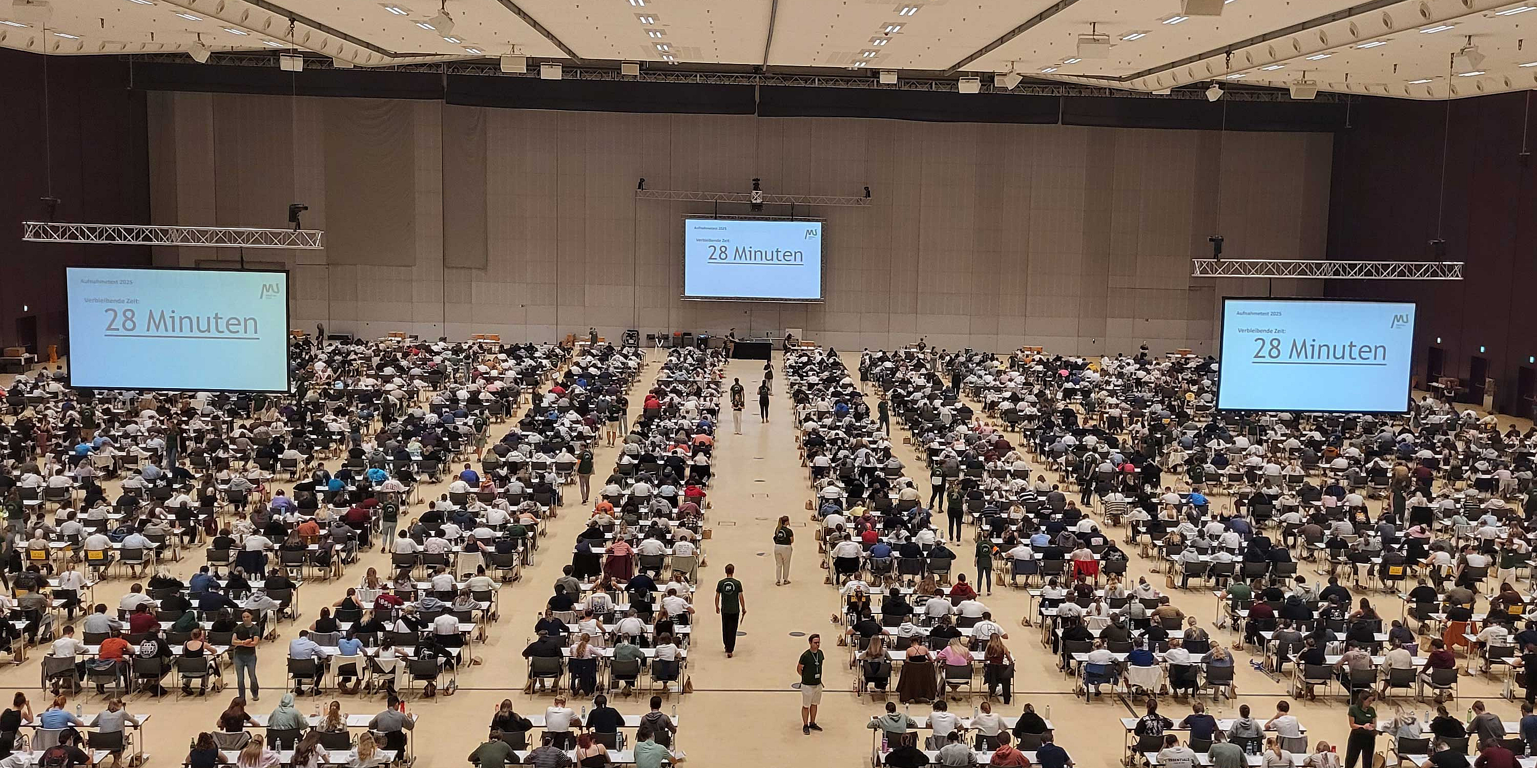 Teilnehmer*innen des MedAT 2025 sitzen in der Grazer Stadthalle an Tischen.