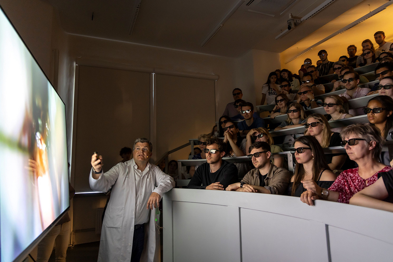 Menschen in einem vollen Hörsaal lauschen einem Vortrag un tragen dabei 3D-Brillen.