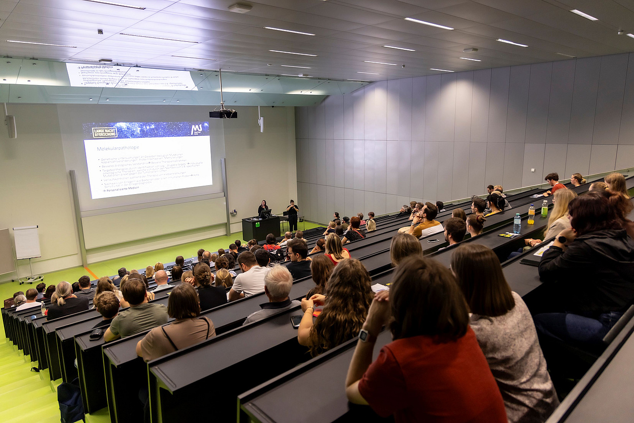 Zuhörer in einem vollen Hörsaal hören einem Vortrag zu.