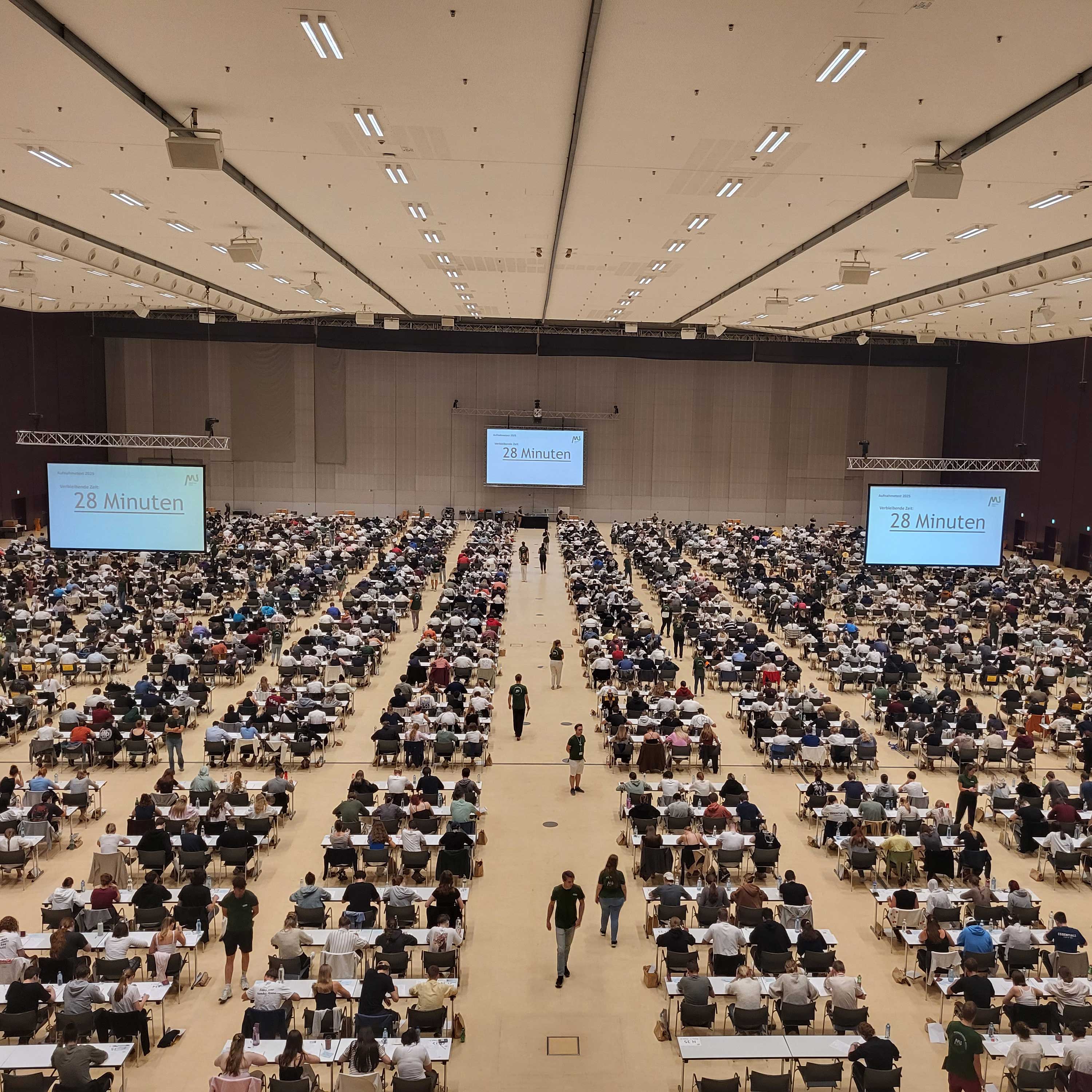 Teilnehmer*innen des MedAT 2025 sitzen in der Grazer Stadthalle an Tischen.