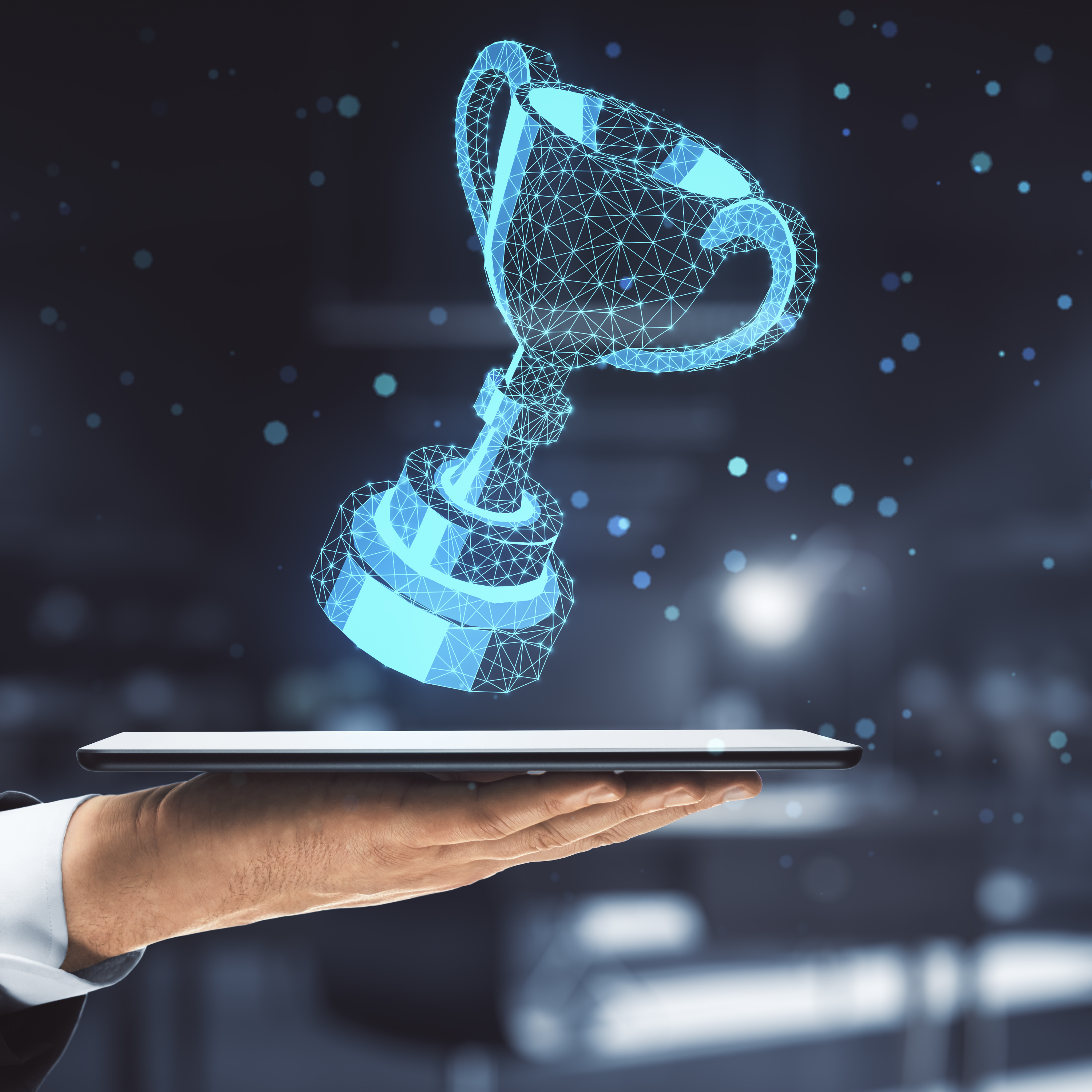 Eine Hand hält ein Tablet über dem ein 3D-Hologramm eines Pokals schwebt